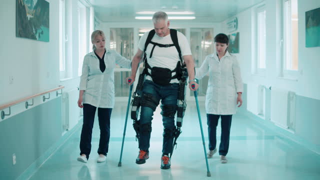 Doctors are helping a male patient in the exoskeleton to walk