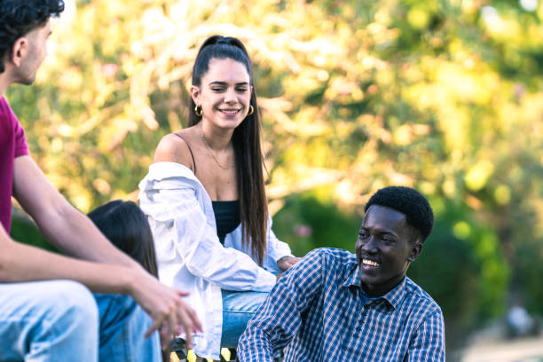 istock Afro man smiling while talking to his friends sitting on a bench in a park 1347551994