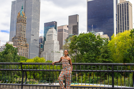 A traveler, dressing in a strapless fashionable, contemporary style dress top and pants, is standing in the front of high buildings of New York\