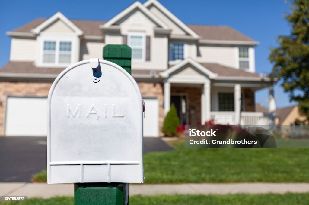 traditional metal mailbox in front of a house Close up isolated image of a white painted metal mail box in front of a single family suburb house with a green lawn. Concept image for mail dalivery and postal service Blue Stock Photo