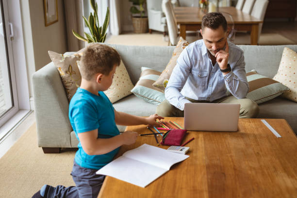 istock Caucasian father using laptop while son doing his homework at home 1347558848