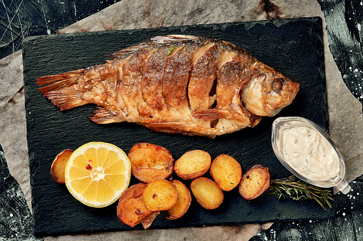 Grilled whole fish Served with baked potatoes, lemon and sauce. Top view