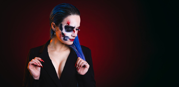 Woman with halloween style skull makeup, with blue hair on red and black background looking to the side and down