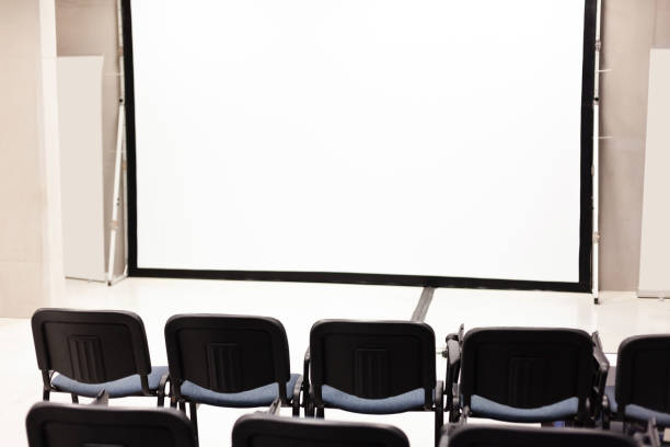 istock Rows of office chairs in front of a blank corporate multimedia presentation screen, vacant conference room interior, empty auditorium, public event, employee training, education, nobody, copy space. 1347560314