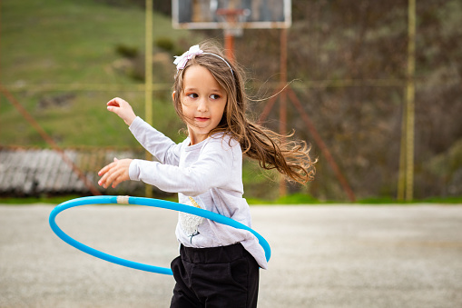 Girl playing with a hula hoop in a school's basketball court in the village.