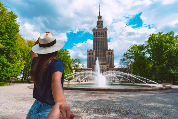 Follow me. Young tourist woman in white sun hat holding her boyfriend by hand and walking in Warsaw city. Couple on summer holiday vacation in Poland. Traveling together. Follow me. Young tourist woman in white sun hat holding her boyfriend by hand and walking in Warsaw city. Couple on summer holiday vacation in Poland. Traveling together. High quality photo warsaw stock pictures, royalty-free photos & images