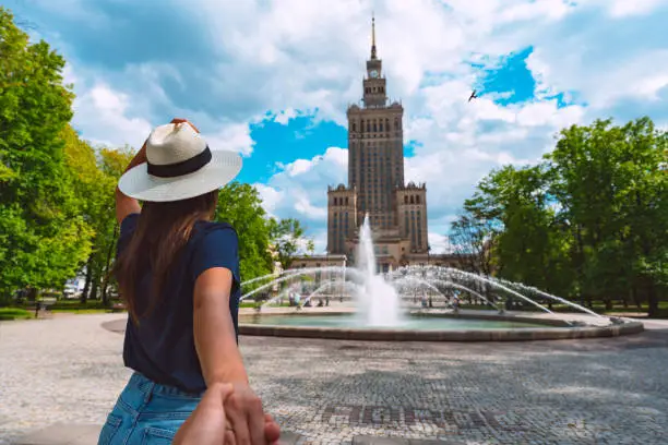 Follow me. Young tourist woman in white sun hat holding her boyfriend by hand and walking in Warsaw city. Couple on summer holiday vacation in Poland. Traveling together. High quality photo