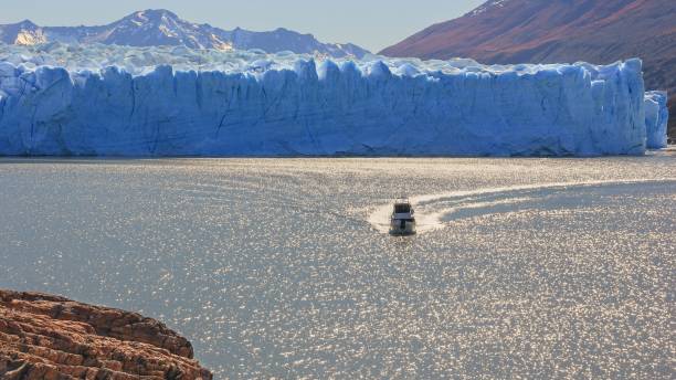 panoramic view to glacier landscape with tourist boat sailing on dazzle blurred surface of lake in sun glare near famous melting perito moreno glacier, in patagonia, argentina. - floe lake imagens e fotografias de stock