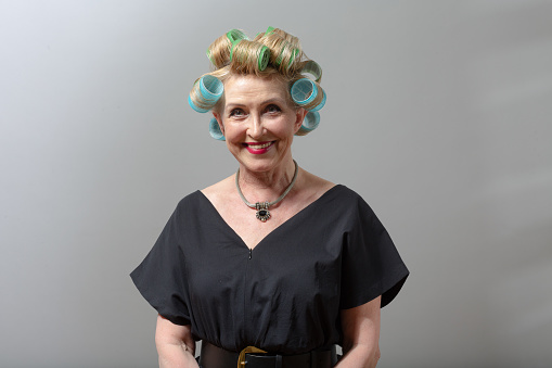 Elderly old aged woman smiling housewife with curlers rollers on hair head.