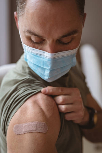 kaukasischer mann mit gesichtsmaske, der seine geimpfte schulter zu hause zeigt - isolated cold virus head and shoulders cold and flu stock-fotos und bilder