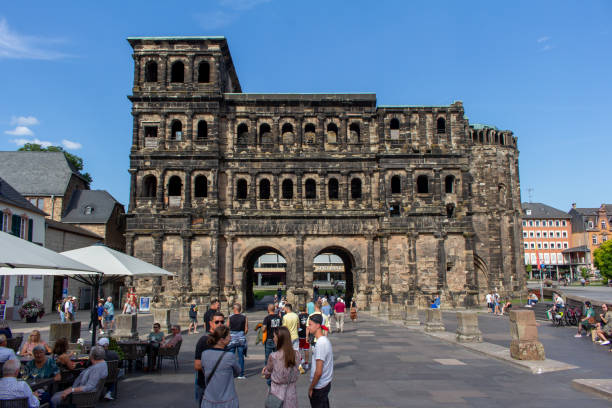 Trier, Germany - September 5, 2021: Tourists and local citizens enjoy a sunny Autumn day in front of the ancient Porta Nigra (Black Gate), built in 170 AD. The gate is the largest Roman city gate north of the Alps. It is part of the Trier Roman Monuments, and is a UNESCO World Heritage Site.