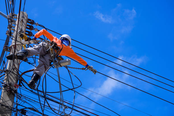 istock Electrician with safety equipment and various work tools is installing cable lines and electrical system on electric power pole against blue sky 1347607788
