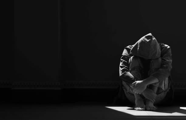 luz e sombra na superfície de um homem sem esperança sentado sozinho abraçando os joelhos no chão em sala escura vazia - solitary confinement - fotografias e filmes do acervo