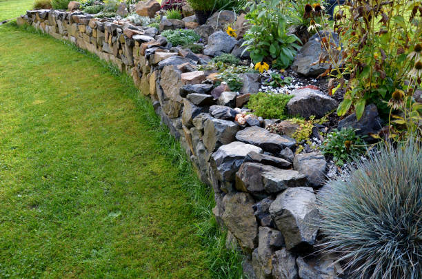 la pared seca sirve como terraza para el jardín, donde contiene una masa de tierra. la pared está ligeramente curvada, lo que ayuda a que se estabilice mejor. plantación de plantas perennes y jardines de rocas - pared de piedra fotografías e imágenes de stock