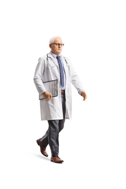 scatto a figura intera di un medico maschio maturo che cammina e tiene in mano una clipboard - doctor male doctor mature men portrait foto e immagini stock