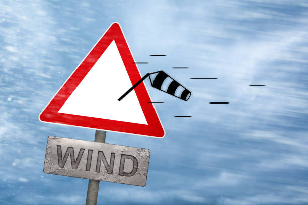 Wind warning sign getting blown away by a storm High winds concept with a triangular road warning sign. The pictogram is getting blown off the sign itself. gale stock pictures, royalty-free photos & images
