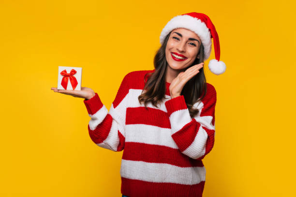 istock Cute excited smiling woman with Christmas gift box in hands is having fun while posing on yellow background 1347624584