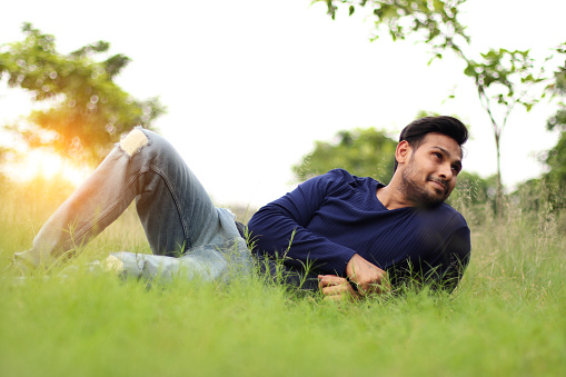 Young handsome Indian man laying in grass and he looking away outdoors in the nature.