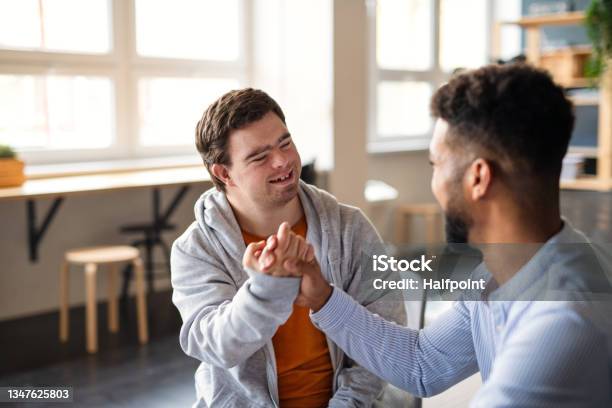 Young Happy Man With Down Syndrome With His Mentoring Friend Celebrating Success Indoors At School Stock Photo - Download Image Now
