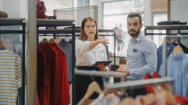 istock Clothing Store: Businesswoman Uses Tablet Computer, Talks to Visual Merchandising Specialist, Collaborate To Create Stylish Collection. Small Business Fashion Shop Sales Manager Talks to Designer 1347626122