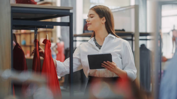 tienda de ropa: empresaria y especialista en visual merchandising utiliza el teléfono inteligente para crear una colección elegante. fashion shop sales retail manager comprueba el stock. propietario de una pequeña empresa y trabajos de diseño - clothing store fotos fotografías e imágenes de stock