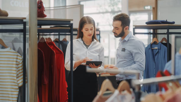 istock Clothing Store: Businesswoman Uses Tablet Computer, Talks to Visual Merchandising Specialist, Collaborate To Create Stylish Collection. Small Business Fashion Shop Sales Manager Talks to Designer 1347626137