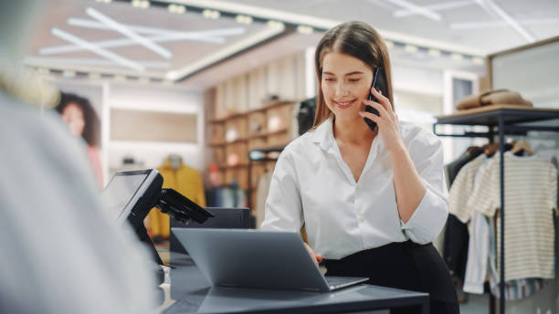 magasin de vêtements modernes: un spécialiste du support client amical parle au client sur le smartphone. un directeur des ventes au détail souriant ou un jeune designer contacte le client à propos de la commande en ligne dans un magasin de mode - supermarket discussion people talking photos et images de collection