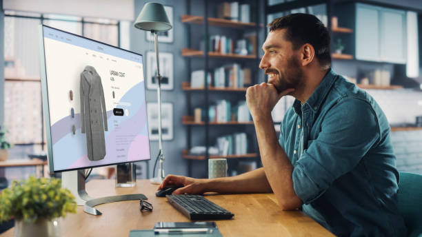 istock Handsome Caucasian Specialist Using Desktop Computer with Clothing Online Web Store to Choose and Buy New Stylish Coat. Happy Man Browsing Over the Internet at Home Living Room. 1347626332