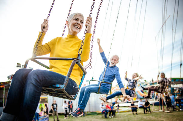 istock Happy senior friends having fun while riding on chain swing at amusement park. 1347627011