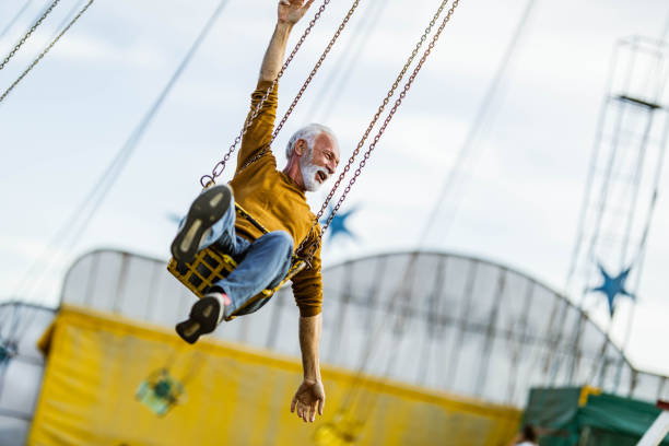 istock Happy mature man riding on chain swing at amusement park. 1347627285
