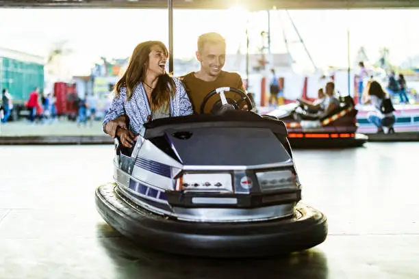 Happy couple having fun while driving bumper car at amusement park.