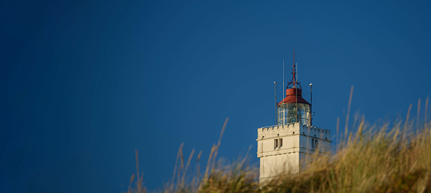 Banner of lighthouse with dunes. BlåvandLighthouse against blue sky with dune at the Danish North Sea coast in vintage style, Blåvandshuk Fyr, Jutland, Denmark, Europe.