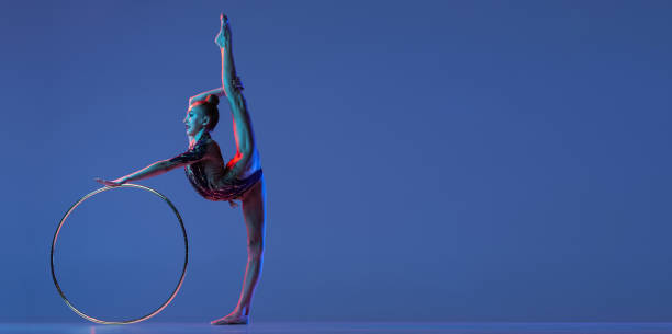 istock Flyer with young rhythmic gymnastics artist standing in twine isolated on blue studio background in pink neon light. Concept of sport 1347632045