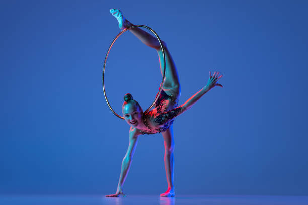 istock Young rhythmic gymnastics artist isolated on blue studio background in pink neon light. Concept of sport 1347632055