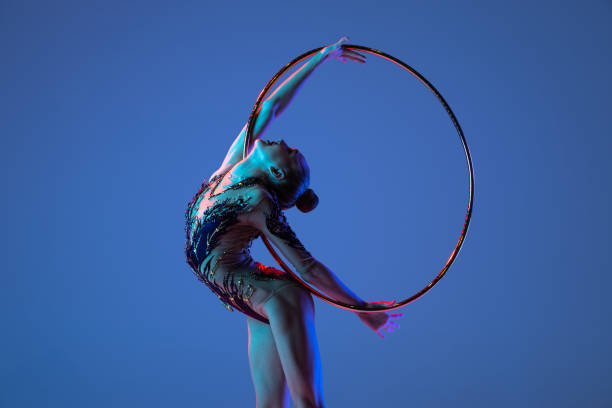 istock Young rhythmic gymnastics artist isolated on blue studio background in pink neon light. Concept of sport 1347632083