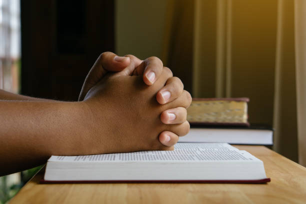 istock Prayer hands on a Holy Bible on wood table with window light.christian backgound 1347634816