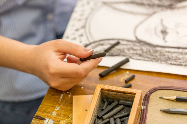 young girl doing a sketch of natural charcoal on paper. table of the artist with different painting supplies - drawing sketch artist charcoal drawing imagens e fotografias de stock