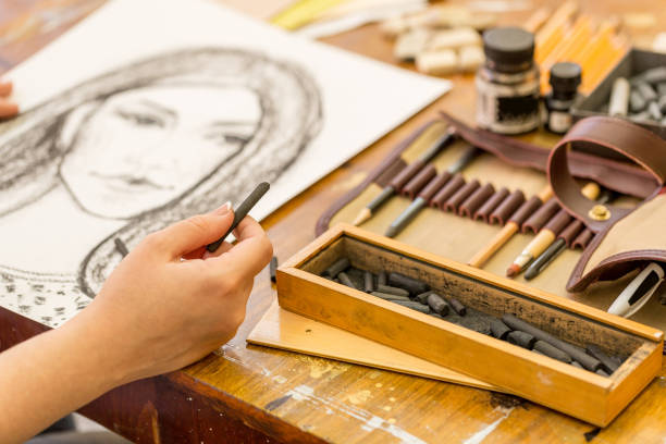 young girl doing a sketch of natural charcoal on paper. table of the artist with different painting supplies - drawing sketch artist charcoal drawing imagens e fotografias de stock