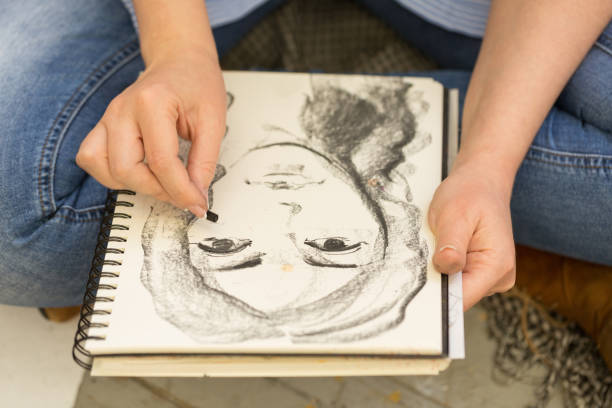 young girl doing a sketch of natural charcoal on paper. table of the artist with different painting supplies - drawing sketch artist charcoal drawing imagens e fotografias de stock