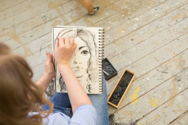 young girl doing a sketch of natural charcoal on paper. table of the artist with different painting supplies - drawing sketch artist charcoal drawing imagens e fotografias de stock