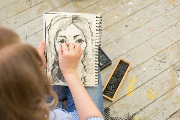 young girl doing a sketch of natural charcoal on paper. table of the artist with different painting supplies - drawing sketch artist charcoal drawing imagens e fotografias de stock