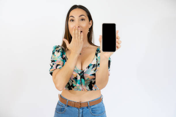 istock Surprised woman is showing a mobile phone standing on white background. 1347636636