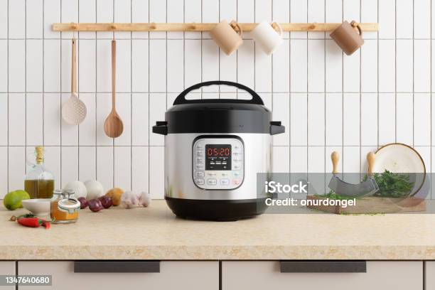 Multi Cooker On Kitchen Counter With Onions Garlic Cooking Oil And Cutting Board Stock Photo - Download Image Now