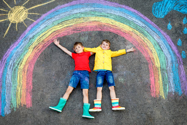 istock Two happy school boys having fun with with rainbow picture drawing with colorful chalks on asphalt. Siblings, twins and best friends painting on ground together. Sign against corona virus. 1347642305