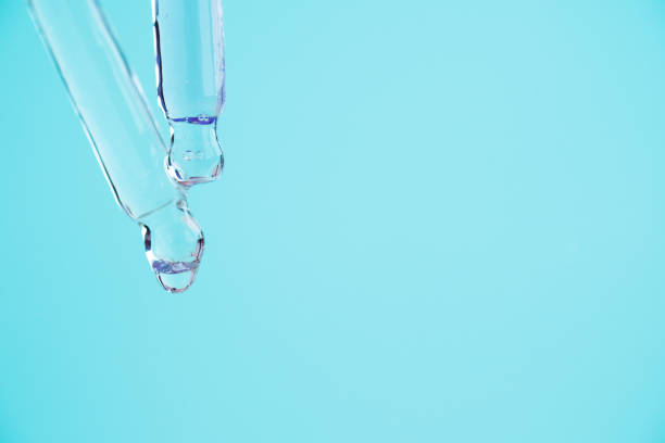 istock Transparent glass pipettes with a serum liquid dripping on blue background 1347643233