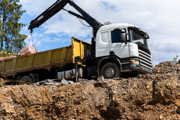 Side bottom pov big modern truck with mounted self loading crane arm boom unloading pallet of new bricks at countryside rural forest suburban construction site. Building materials delivery service