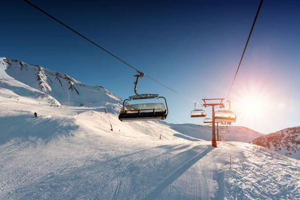 istock Ski lift empty ropeway on hilghland alpine mountain winter resort on bright sunny evening . Ski chairlift cable way with people enjoy skiing and snowboarding. Sunset sky backlit shining on background 1347652033