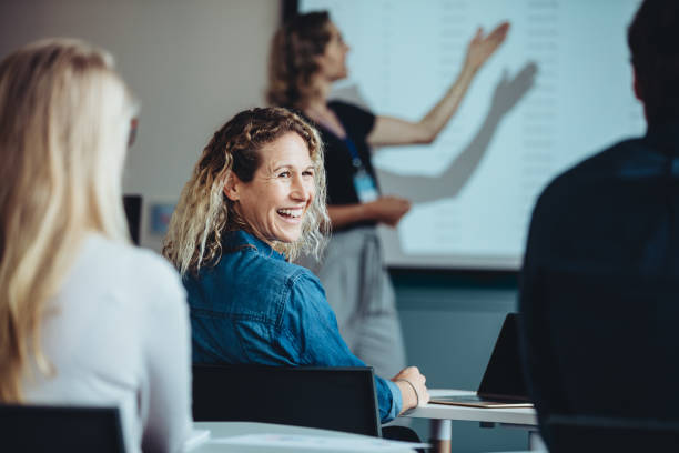 Businesswoman smiling during a presentation Rear view of a woman sitting in audience looking back at a colleague and smiling during a conference. Businesswoman smiling during a presentation. seminar stock pictures, royalty-free photos & images