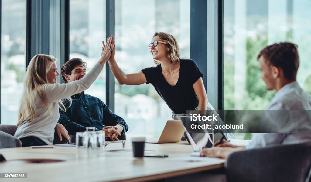 Group of colleagues celebrating success Female professional giving a high five to her colleague in conference room. Group of colleagues celebrating success in a meeting. Business Stock Photo