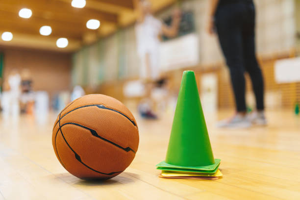 Basketball Training Equipment on Sports Court Wooden Parquet - Basketball Floor. Basketball Training Game.  Close Up on Cones and Ball with Blurred Players and Coach Playing Basketball Practice Game Basketball Training Equipment on Sports Court Wooden Parquet - Basketball Floor. Basketball Training Game.  Close Up on Cones and Ball with Blurred Players and Coach Playing Basketball Practice Game college basketball court stock pictures, royalty-free photos & images